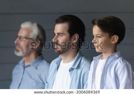 Serious boy, his father and grandpa standing together in row, looking forward. Portrait of three male generations, preschool child, young man, older pensioner. Family relations, heredity concept Royalty-Free Stock Photo #2006084369