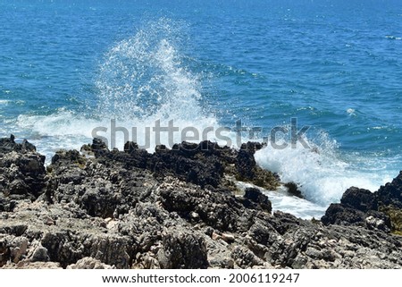 Splashing of waves crashing on stones against background of blue sea