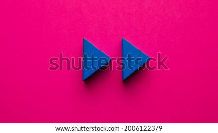 Rewind symbol represented by a triangular blue wooden token on a pink background