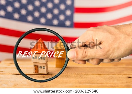 Hand with magnifier and text "best price", wooden house and American flag in the background. Real estate investment