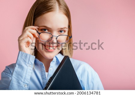 Close up emotional portrait of smiling young woman in glasses with laptop isolated over color pink background with copy space. Teenage girl student or office worker with laptop