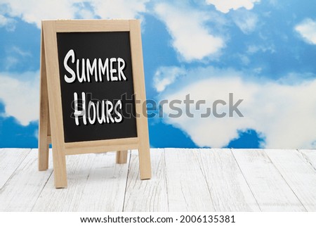Summer hours sign on standing chalkboard on weathered wood with clear sky