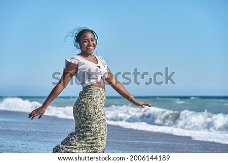 young african american woman listening to music by the shore of the beach