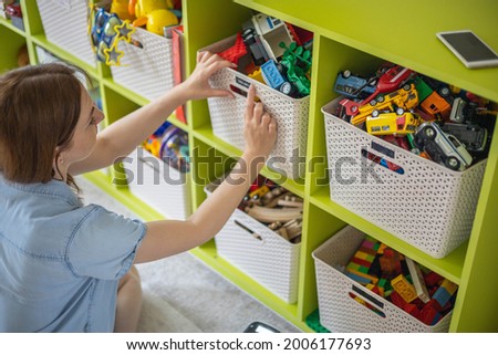 Woman hands applying printing sticker with name title of children toys for comfortable sorting and storage at home. Caring mother organizing domestic space for kids. Housekeeping and household Royalty-Free Stock Photo #2006177693