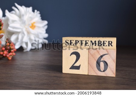 September 26, Date cover design with calendar cube and white Paeonia flower on wooden table and blue background.