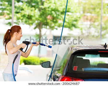 Picture, portrait young, smiling, happy, attractive woman washing automobile at manual car washing self service station, cleaning with foam, pressured water. Transportation, auto, vehicle care concept