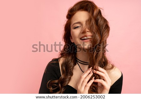 Beautiful red  head woman  with close eyes posing over pink background. Wavy hairs. Perfect smile.  Isolate in studio. 