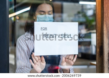 Caucasian Coffee shop owner turns For Rent-For Sale sign in restaurant. Beautiful Waitress woman wear mask and shut down small business due to financial crisis from COVID-19 lockdown and quarantine.