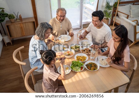 Asian Big happy family spend time have lunch on dinner table together. Little kid daughter enjoy eating foods with father, mother and grandparents. Multi-Generation relationship and activity in house Royalty-Free Stock Photo #2006269856