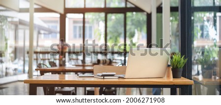 Close up view of co-working space table at cafe with laptop, stationery and blurry cafe interior in the background Royalty-Free Stock Photo #2006271908