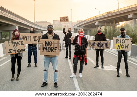 Group of young multi-ethnic people in cloth masks standing on road while protesting on street