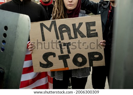 Close-up of woman with dreads holding Make Stop cardboard banner while standing in crowd during rally