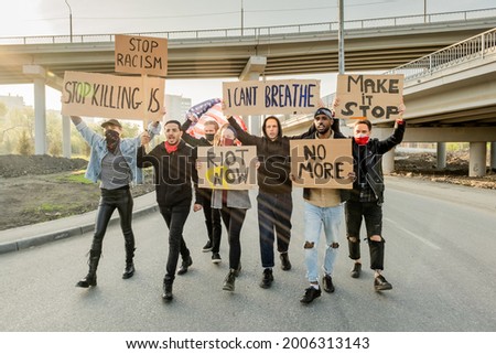 Group of angry young multi-ethnic people raising cardboard banners while protesting against racism at street demonstration