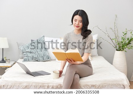 Asia Korean woman sitting on the bed. reading a book or cup of a tea 