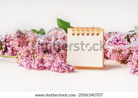 A beautiful floral composition and an empty paper notepad for text. Floral spring background with lilac. Copy space