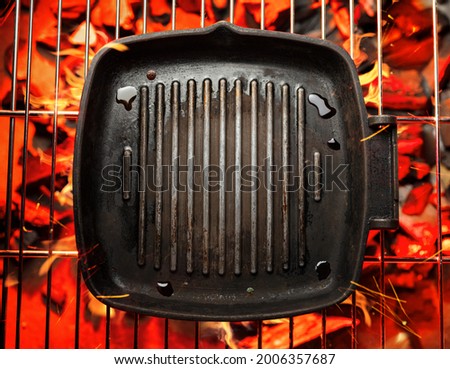Frying pan on bbq grate over hot pieces of coals. Top view.
