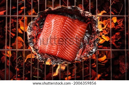 Salmon in aluminum foil on bbq grate over hot pieces of coals. Top view.