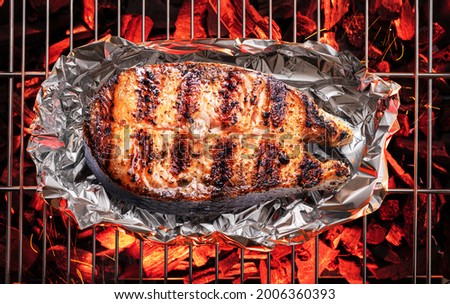 Grilled salmon steak on bbq grate over hot pieces of coals. Top view.