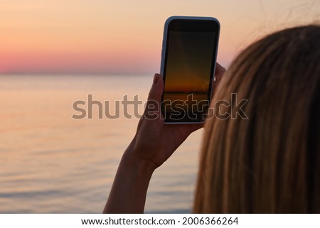 The girl holds a mobile phone in her hands and takes pictures of the sea at dawn. Focus on the phone screen. Make memories using your smartphone. Mobile phone close up