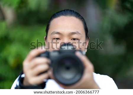 Focus on the Asian man face that he holds the blur Medium Format Camera in his hand and prepare to shoot in front of him.