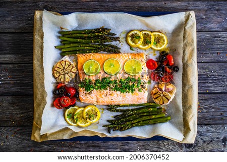 Sheet pan dinner - roasted salmon steak with asparagus, lemon ,rosemary, tomatoes, onion and garlic on cooking pan on wooden table 
