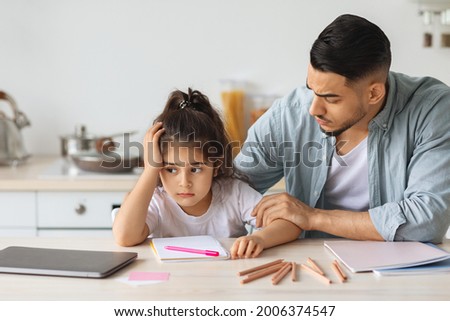 Young arab man single father comforting his upset little daughter, sitting at table with colorful pencils and notebook at kitchen, bored girl kid with unhappy face expression looking at copy space