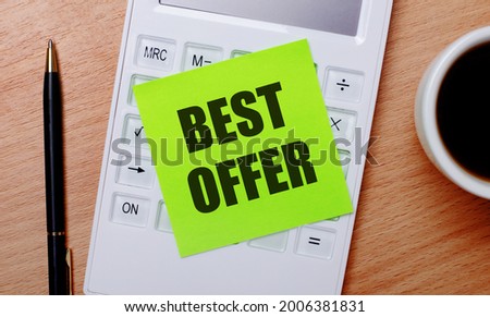 On a wooden table there is coffee in a white cup, a pen and a white calculator with a green sticker with the text BEST OFFER. Business concept
