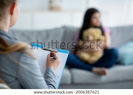 Teenage depression. Psychologist working with upset teen girl at office, talking to her patient, taking notes, selective focus. Unhappy adolescent having consultation with psychotherapist, copy space Royalty-Free Stock Photo #2006387621