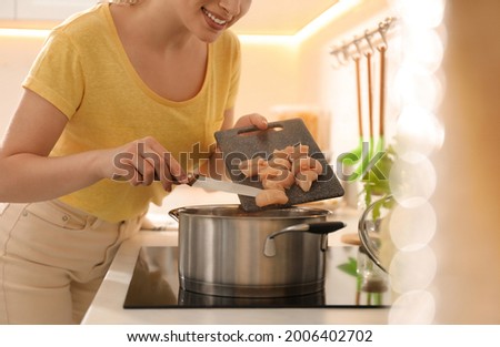 Woman putting meat into pot to make bouillon in kitchen, closeup. Homemade recipe