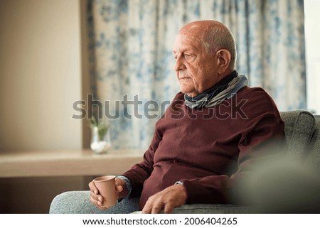 Depressed senior man sitting on armchair holding disposable cup of coffee and thinking. Frustrated retired man sitting on sofa. Sad mature man sitting alone at nursing home with sad expression. Royalty-Free Stock Photo #2006404265