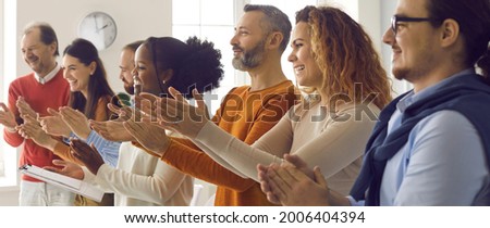 Happy diverse audience clapping hands. Group of excited smiling young and mature people applauding coach, teacher or instructor thanking speaker for interesting, engaging and fun casual presentation Royalty-Free Stock Photo #2006404394