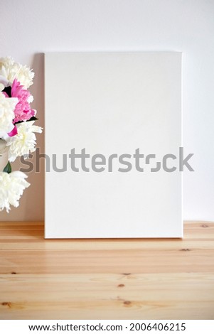 Canvas mockup with pink flowers on wooden table on white wall background. Blank artistic canvas