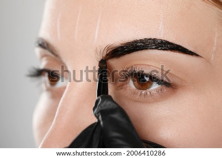 Beautician applying tint during eyebrows correction procedure on grey background, closeup