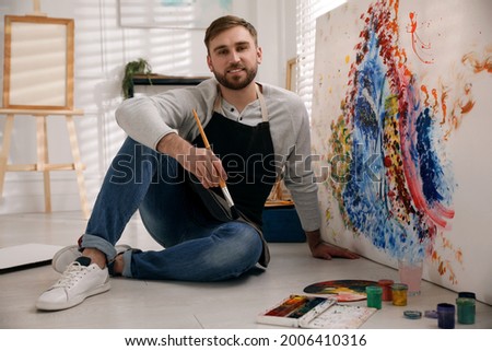 Young man with painting brush near canvas in artist studio