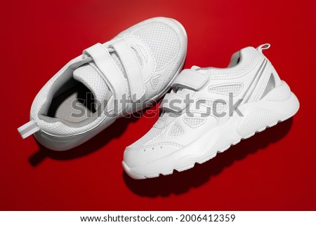 top view two white new children's sneakers with Velcro for easy footwear on a red background, one sneaker on the side.