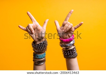 Hand gestures. Thumbs up, that's a cool gesture of the rocker. women's hand with lots of bracelets, youth fun style. bright yellow background