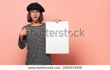 young woman artist feeling happy, surprised and proud, pointing to self with an excited, amazed look