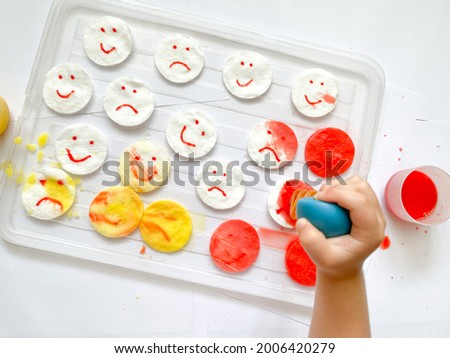 The study of emotional intelligence. Children's emotions. Children's hands with yellow and red emoticons. Montessori concept. The child draws with paints. Fine motor skills. Children's experiences. Royalty-Free Stock Photo #2006420279