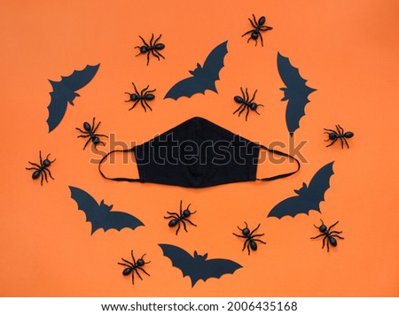 Black face mask and Halloween pattern with black decorations on an orange background. Black paper bat, ants and eyes, Halloween party decorations at pandemic coronavirus