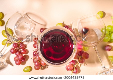 Glasses of red and white wine with sunshine and shadows, with bottle and decanter, bunch of grapes, on creamy color background, flatlay top view Wine tasting, autumn harvest, winery concept 