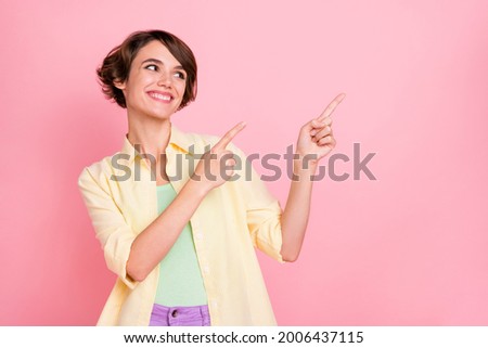 Photo of charming cute young lady dressed yellow shirt looking pointing two fingers empty space isolated pink color background