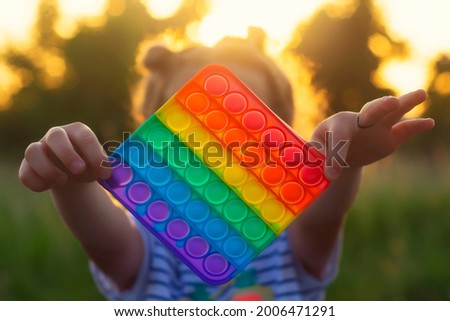 The child plays with a colorful rainbow game of poppit. Silicone fidget close-up