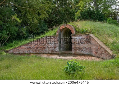 Old ice house burried under a grass mound with red bricks and open gate. Royalty-Free Stock Photo #2006478446