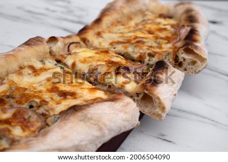 Italian cuisine. Selective focus on a sliced mozzarella cheese pizza with onion and different kinds of cheese on the white marble table.