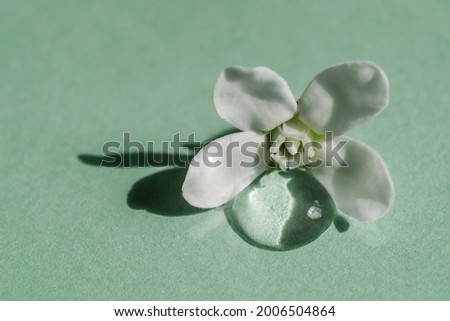 A drop of transparent cosmetic gel with flower on a green background.