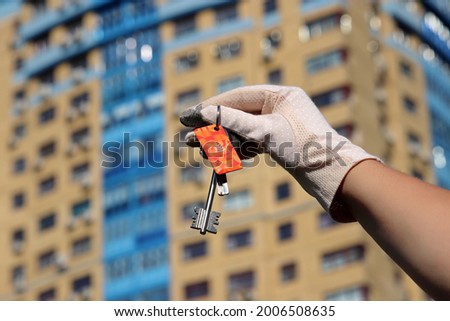 Apartment purchase, woman in protective gloves holding keychain with digital and home keys on background of new buildings. Moving home or renting property during coronavirus pandemic