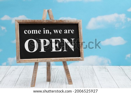 Open sign on standing chalkboard on weathered wood with clear sky