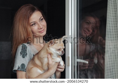 Pretty mature woman with Chihuahua dog in hands on home balcony. Middle aged female and her doggy Chihuahua. Concept pet love and family friend