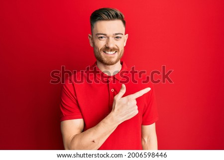 Young redhead man wearing casual clothes smiling cheerful pointing with hand and finger up to the side 