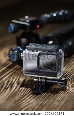 Black small action camera in waterproof case and tripod on brown wooden tabletop.